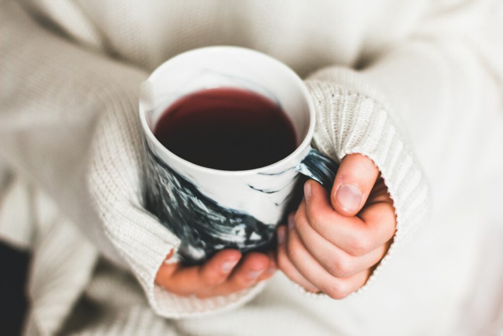 Mains d'une femme enveloppées dans un pull tricoté tenant une tasse de tisane chaude, symbole d'un accompagnement nutritionnel doux pour retrouver l'énergie et réduire la fatigue.