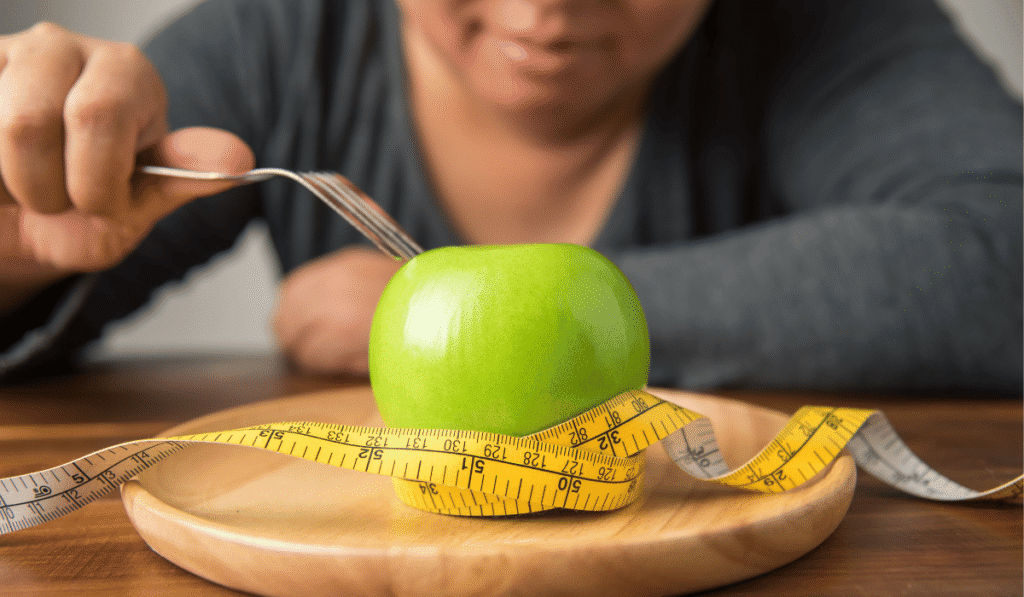 Femme souriante devant une pomme verte entourée d'un mètre ruban dans une assiette en bois, illustrant la perte de gras et l'alimentation.